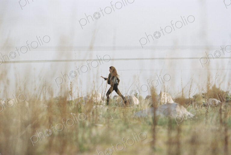 A woman striding across the grass past rocks along the shore of a lake.