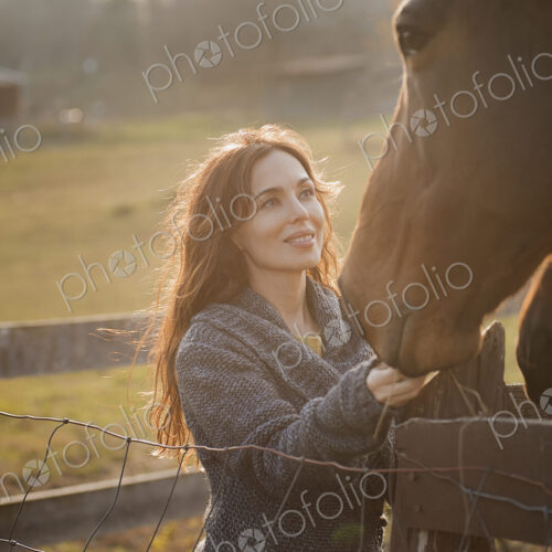 A woman stroking the muzzles of two horses in a paddock on an organic farm. A woman stroking the muzzles of two horses in a paddock on an organic farm.