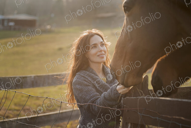 A woman stroking the muzzles of two horses in a paddock on an organic farm.