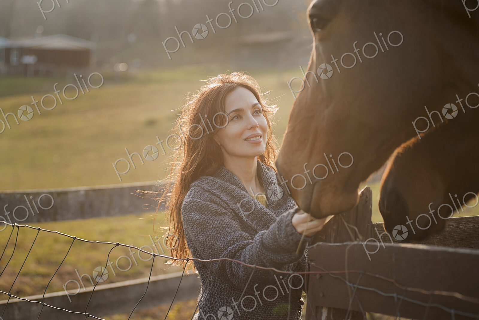 A woman stroking the muzzles of two horses in a paddock on an organic farm.