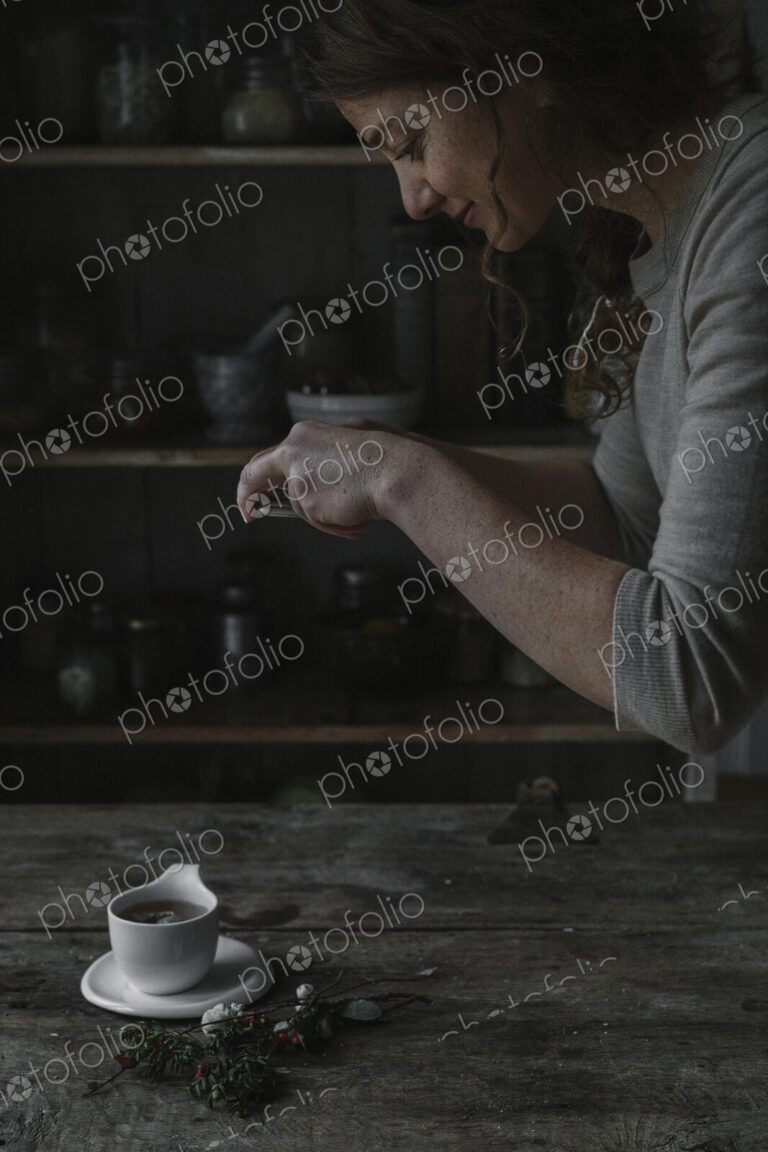 A woman taking a photograph from above of a cup and saucer on a kitchen table.