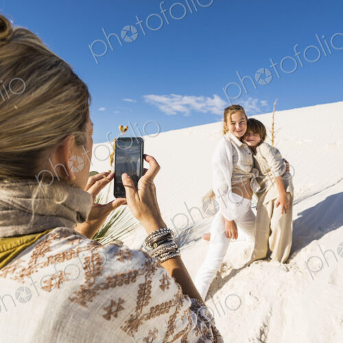 A woman taking picture of her children with a smart phone in white sand dunes… A woman taking picture of her children with a smart phone in white sand dunes…