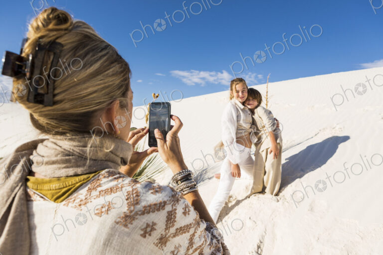 A woman taking picture of her children with a smart phone in white sand dunes…