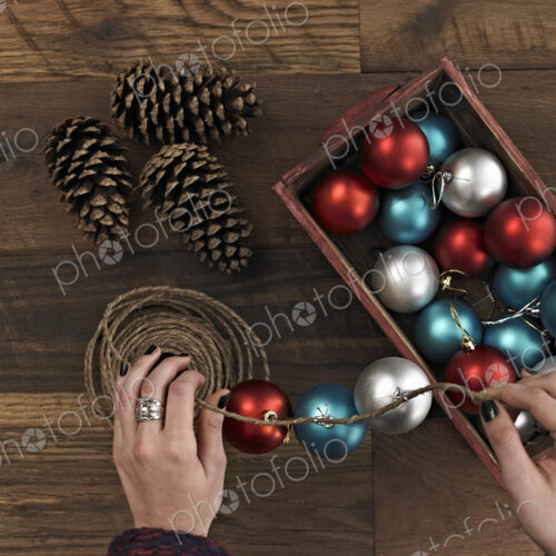 A woman threading Christmas shiny round ornaments on a piece of string. A small group… A woman threading Christmas shiny round ornaments on a piece of string. A small group…