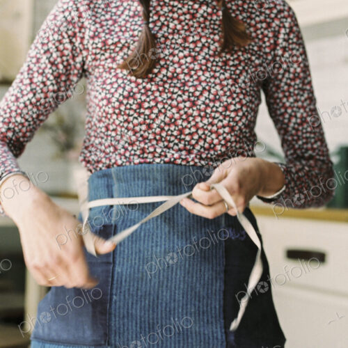 A woman tying the tapes of an apron aroud her waist. A woman tying the tapes of an apron aroud her waist.