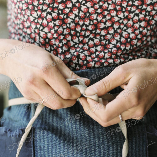 A woman tying the tapes of an apron aroud her waist. A woman tying the tapes of an apron aroud her waist.