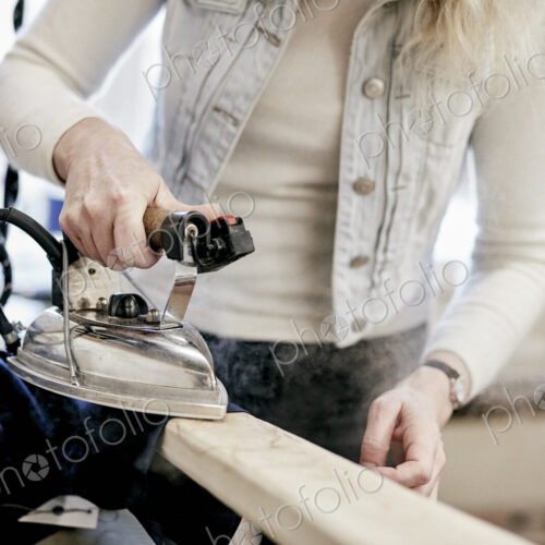 A woman using a steam iron on a new jacket, pressing the newly made garment. A woman using a steam iron on a new jacket, pressing the newly made garment.