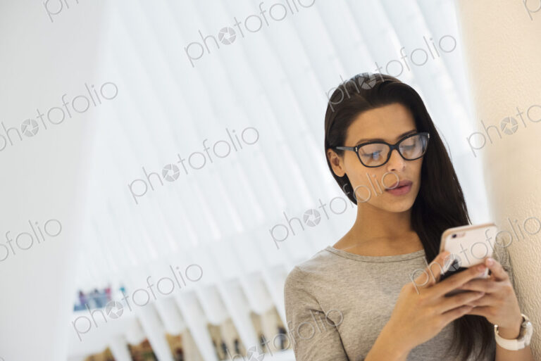 A woman using her smart phone, checking social media and messages, under the atrium…