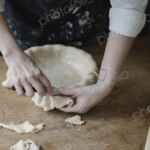 A woman using raw pastry dough to line a pie dish and finish the edge. A woman using raw pastry dough to line a pie dish and finish the edge.