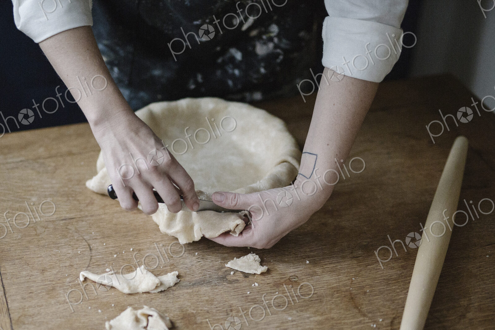A woman using raw pastry dough to line a pie dish and finish the edge.
