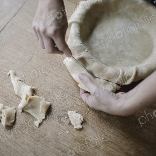 A woman using raw pastry dough to line a pie dish and finish the edge. A woman using raw pastry dough to line a pie dish and finish the edge.
