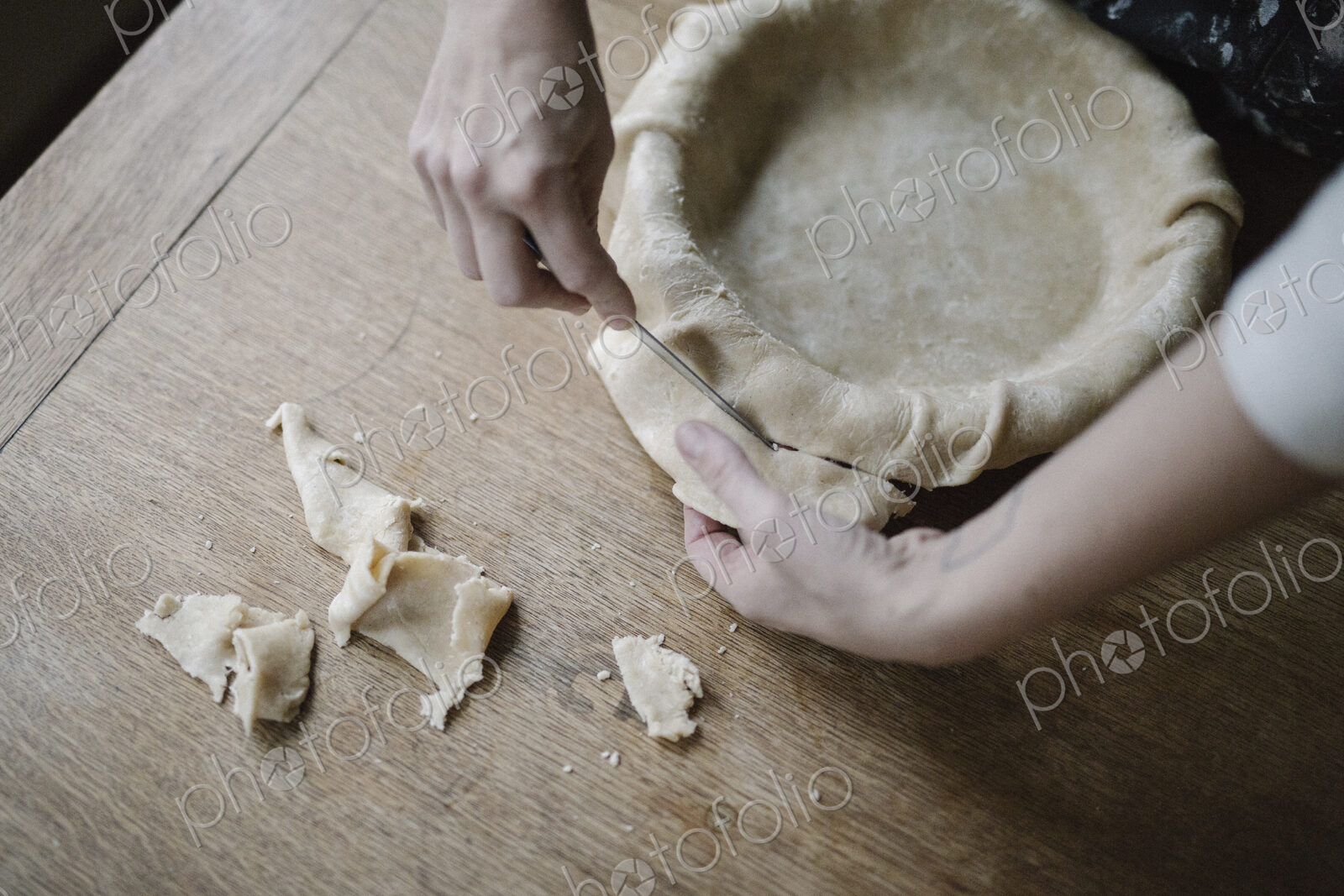 A woman using raw pastry dough to line a pie dish and finish the edge.