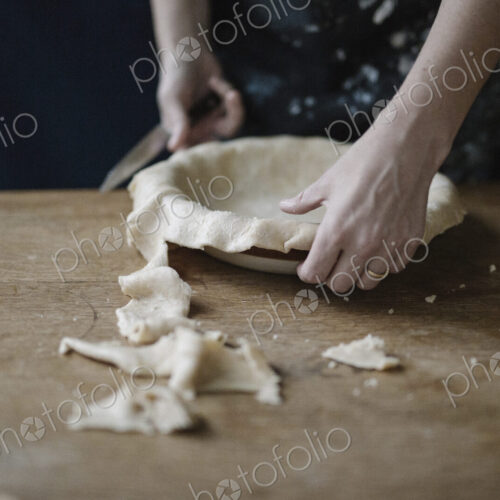A woman using raw pastry dough to line a pie dish and finish the edge. A woman using raw pastry dough to line a pie dish and finish the edge.