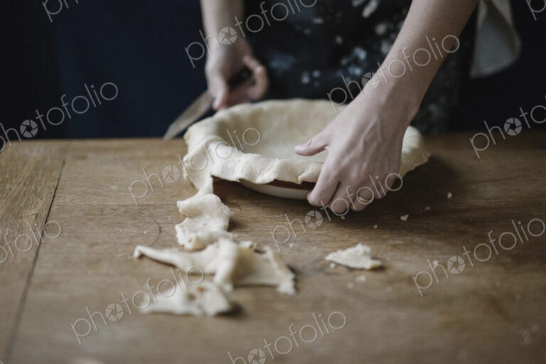 A woman using raw pastry dough to line a pie dish and finish the edge.