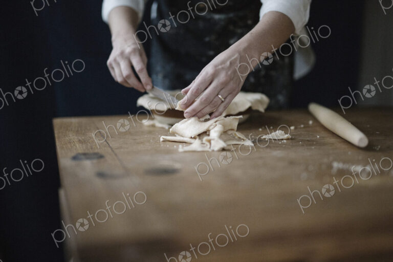 A woman using raw pastry dough to line a pie dish and finish the edge.