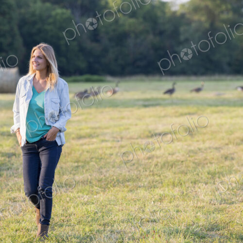A woman walking across a field, away from a flock of geese outdoors in the fresh air.