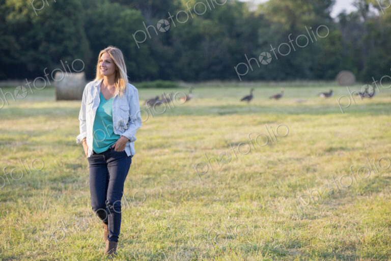 A woman walking across a field, away from a flock of geese outdoors in the fresh air.