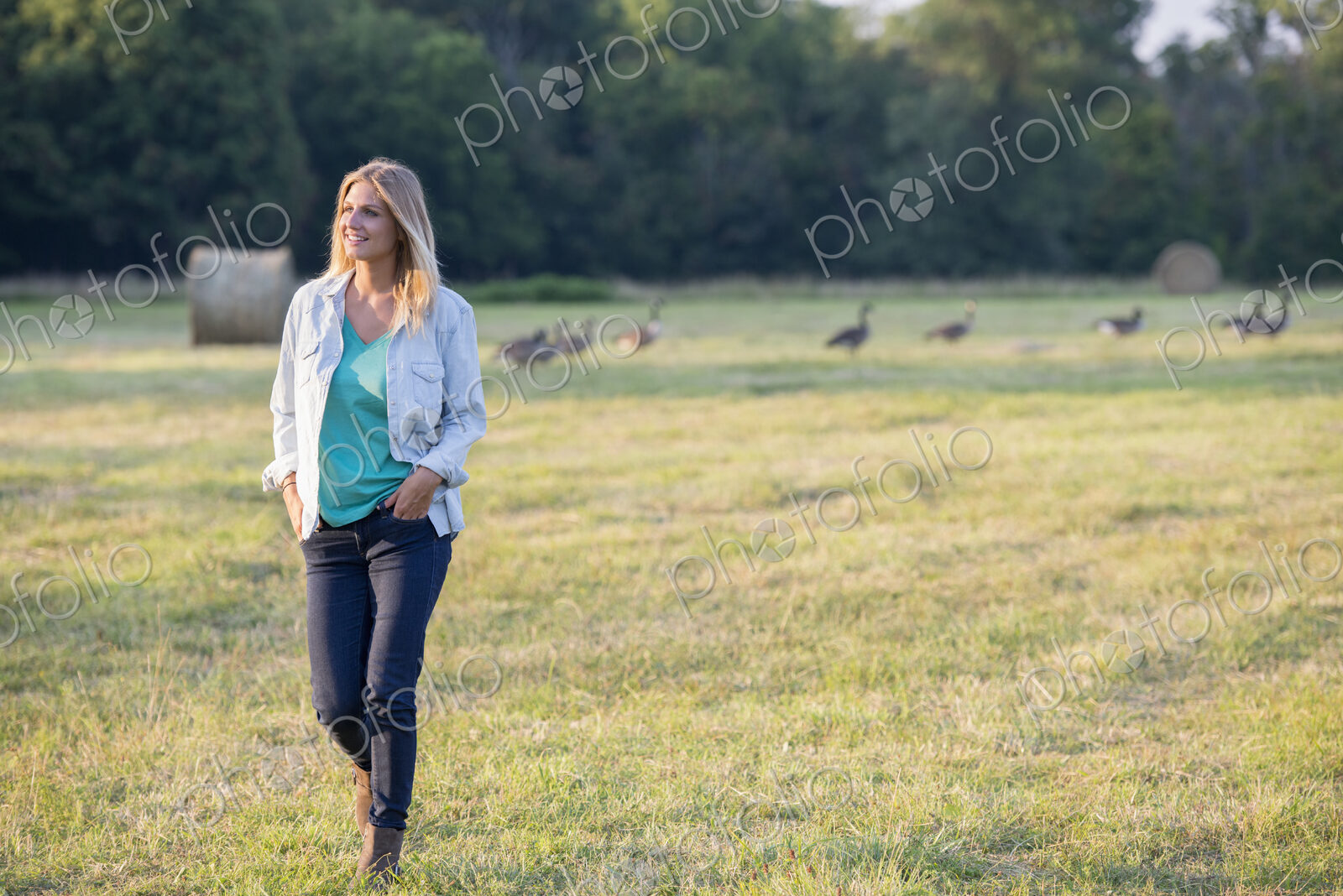 A woman walking across a field, away from a flock of geese outdoors in the fresh air.