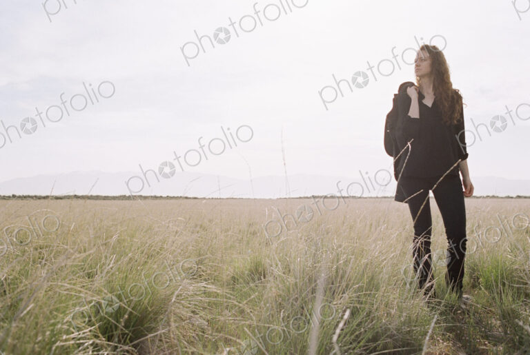 A woman walking across a grassy landscape with a bag over her shoulder.