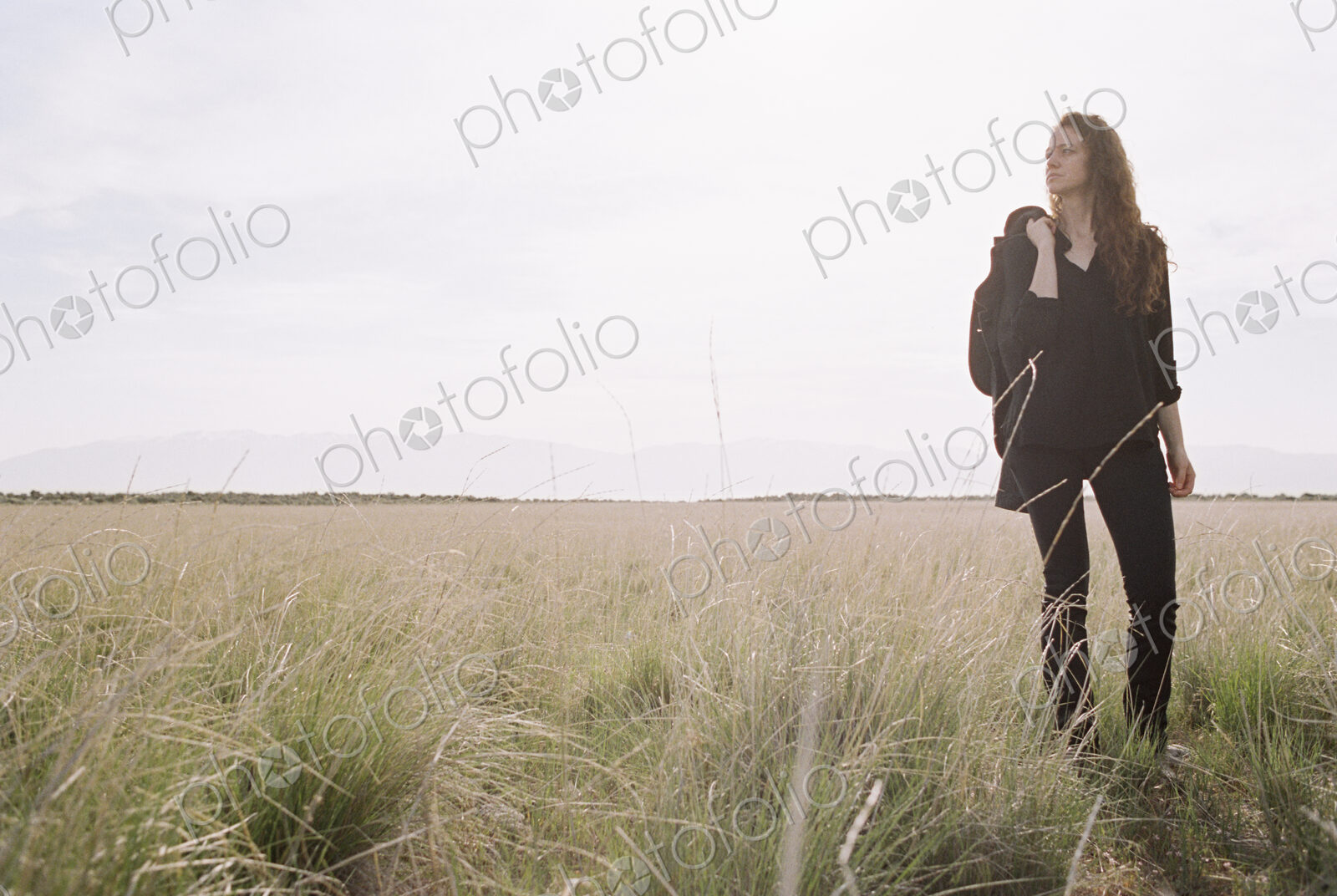 A woman walking across a grassy landscape with a bag over her shoulder.