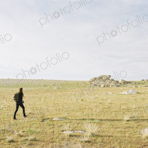 A woman walking across open ground towards a small cairn, carrying a backpack. A woman walking across open ground towards a small cairn, carrying a backpack.