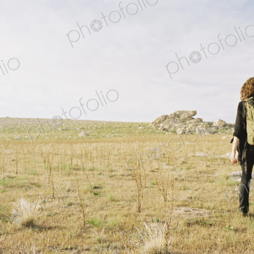 A woman walking across open ground wearing a hat, carrying a backpack. A woman walking across open ground wearing a hat, carrying a backpack.