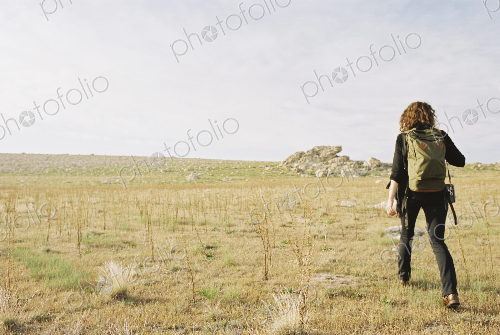 A woman walking across open ground wearing a hat, carrying a backpack.