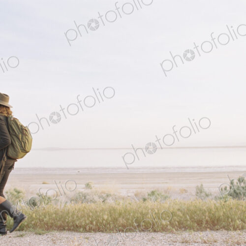 A woman walking along a country road, wearing a hat and carrying a backpack. A woman walking along a country road, wearing a hat and carrying a backpack.
