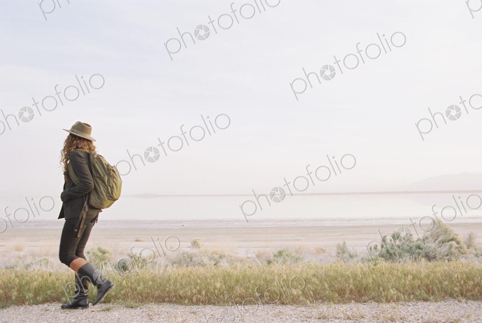 A woman walking along a country road, wearing a hat and carrying a backpack.
