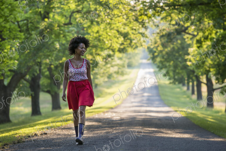 A woman walking down a tree lined path.