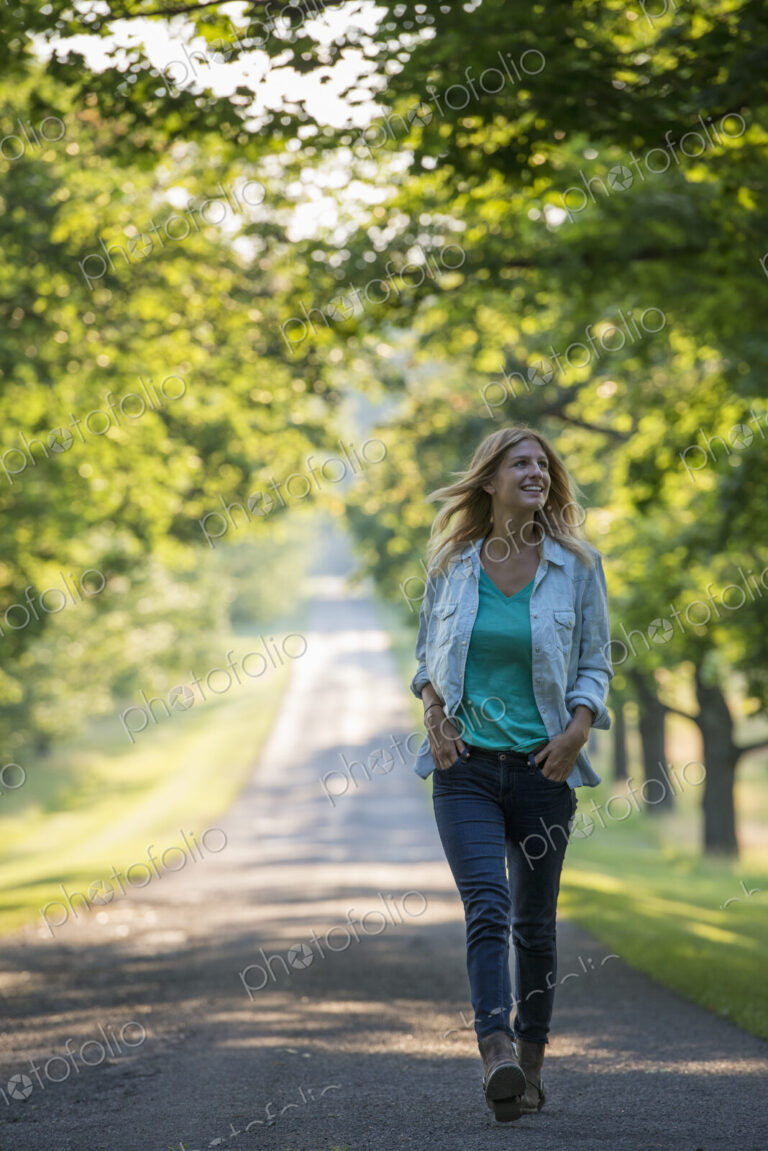 A woman walking down a tree lined path.