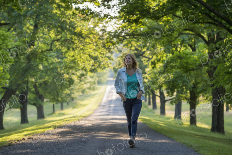 A woman walking down a tree lined path.