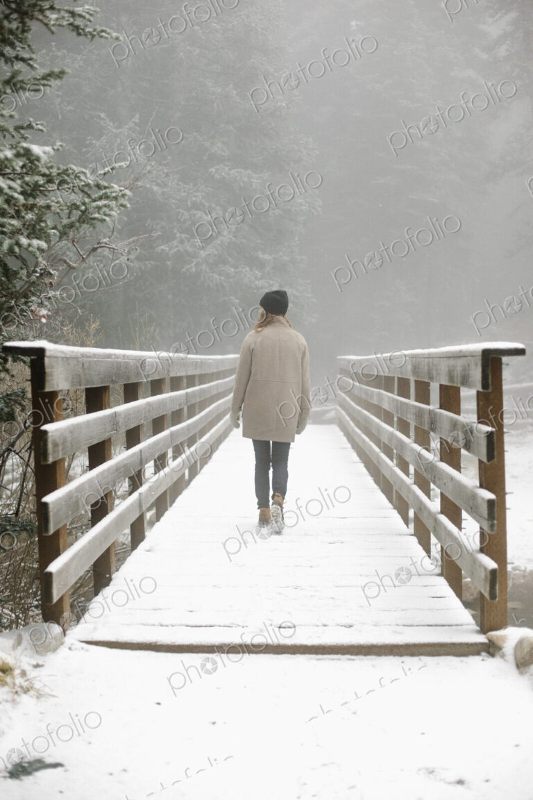 A woman walking on a footbridge in the mountains in snow.
