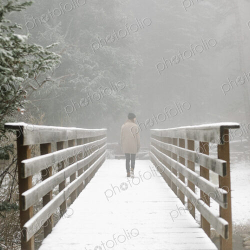 A woman walking on a footbridge in the mountains in snow. A woman walking on a footbridge in the mountains in snow.