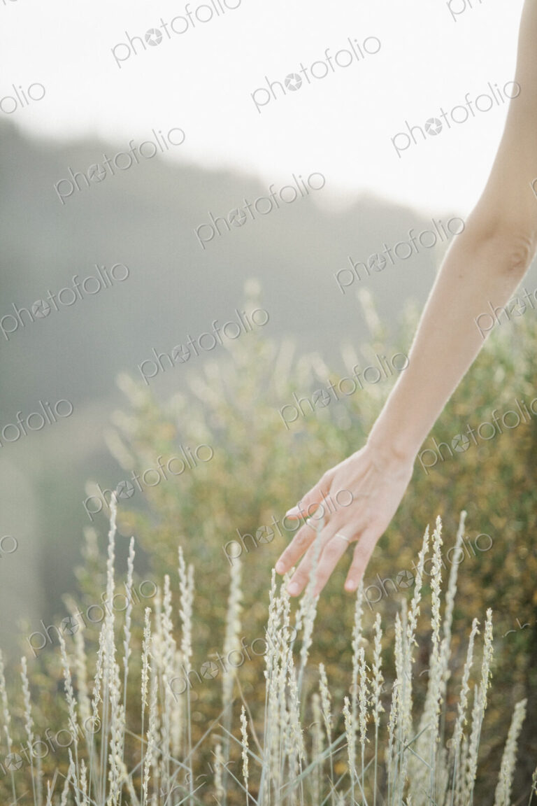 A woman walking through long grass trailing her hand through the stems.