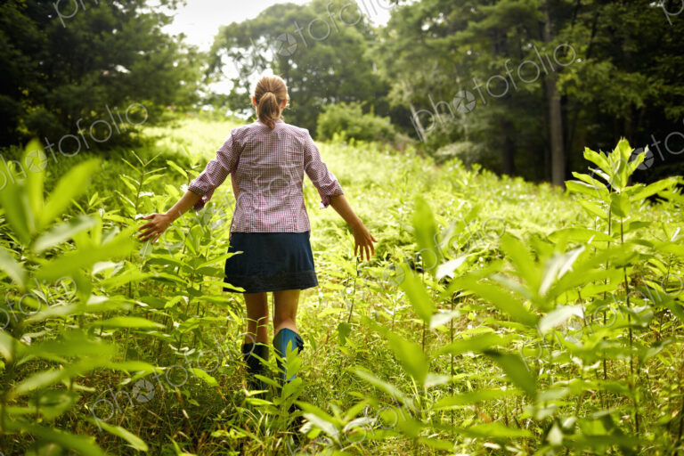 A woman walking through the undergrowth in woodland, with her arms brushing the tops…