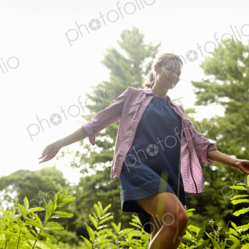 A woman walking through the undergrowth in woodland, with her arms brushing the tops…