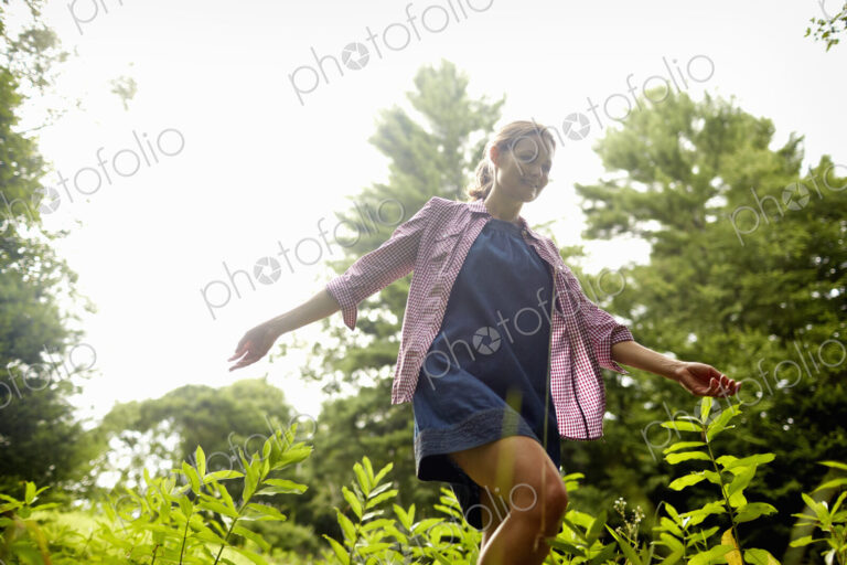 A woman walking through the undergrowth in woodland, with her arms brushing the tops…
