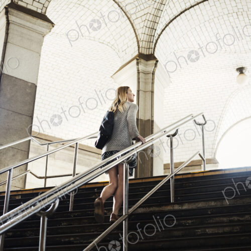 A woman walking up the steps of a subway, travelling in the city.