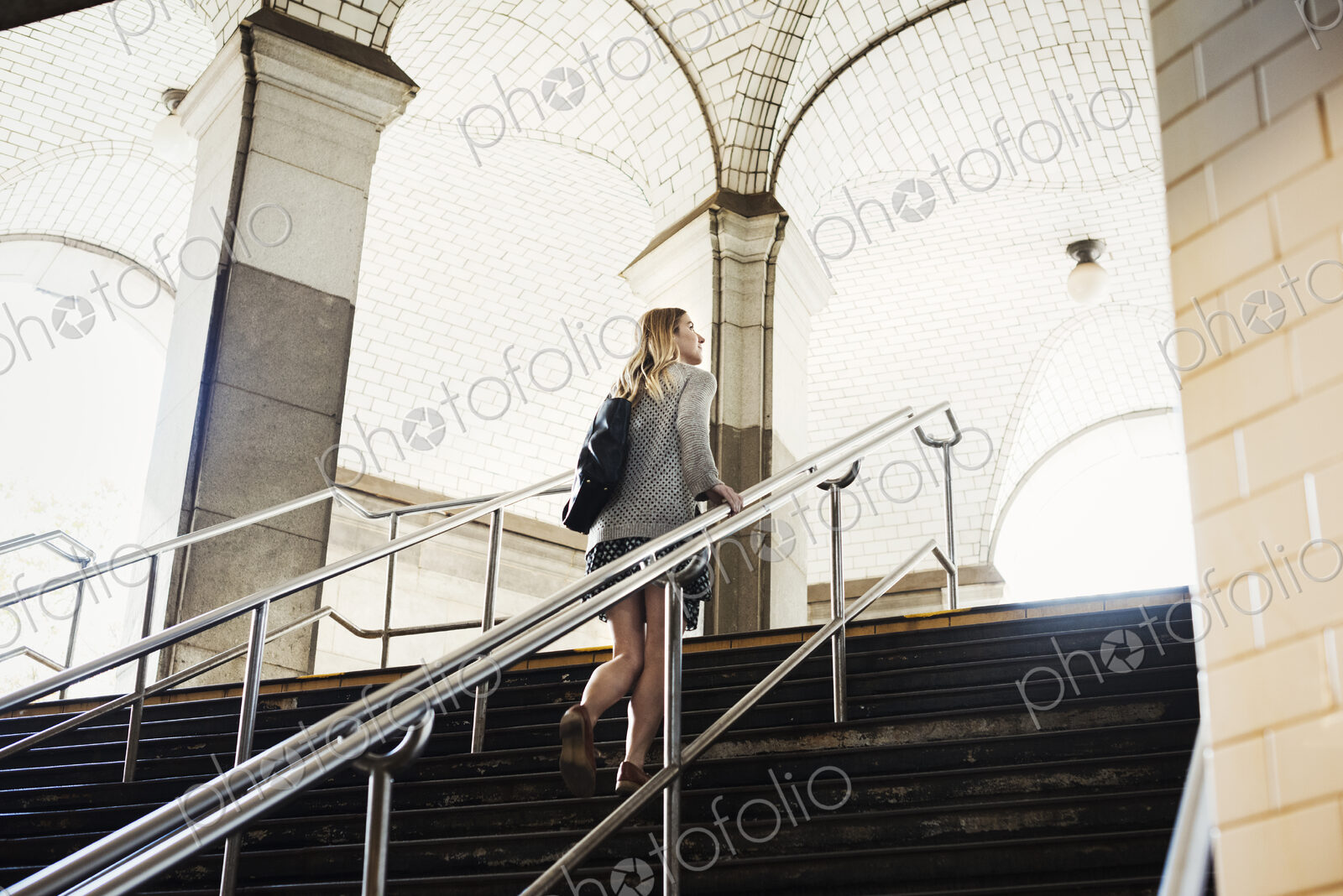 A woman walking up the steps of a subway, travelling in the city.