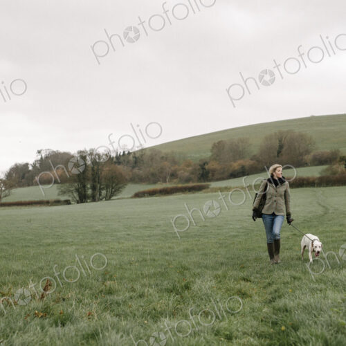 A woman walking with a dog across a grass field. A woman walking with a dog across a grass field.