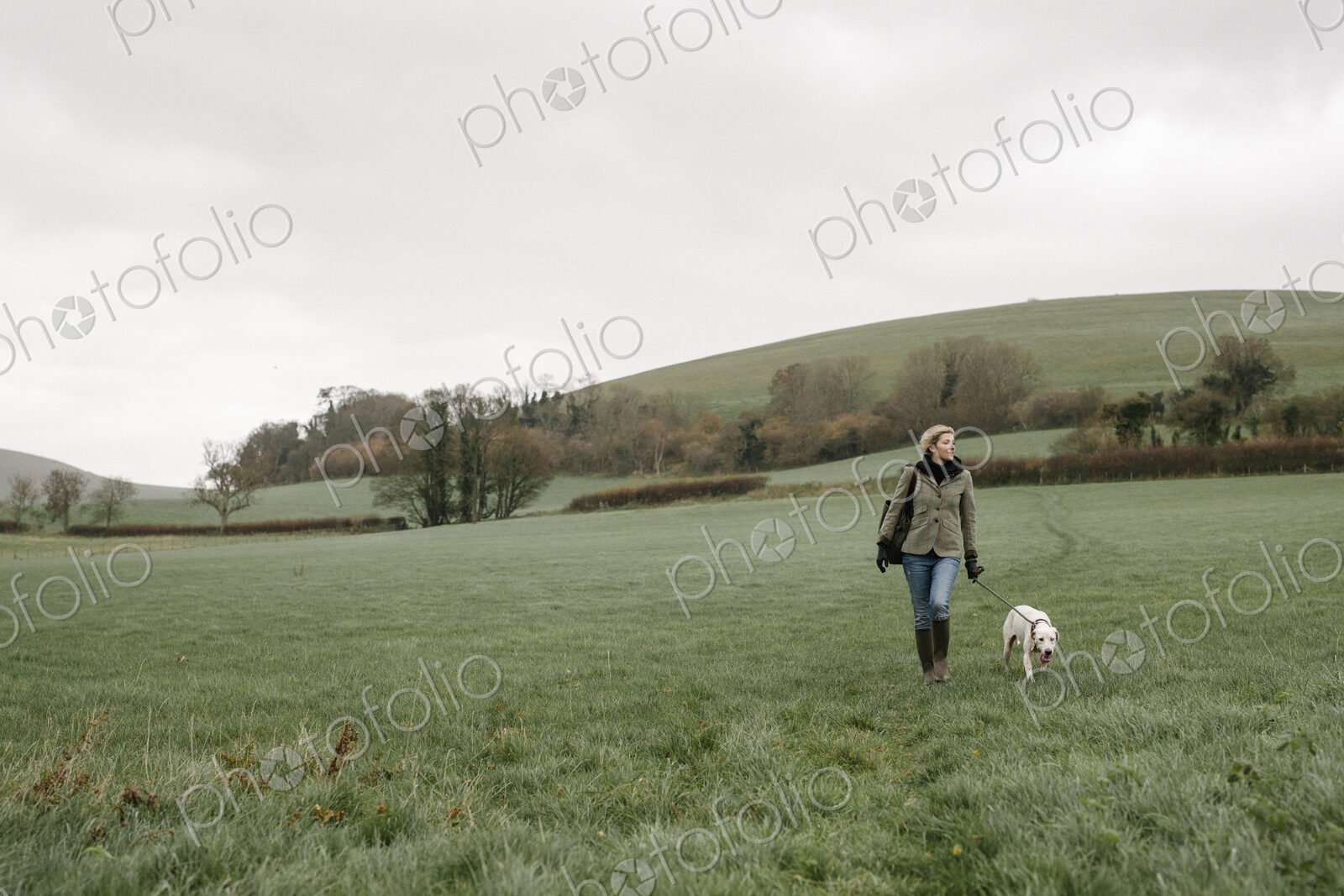A woman walking with a dog across a grass field.