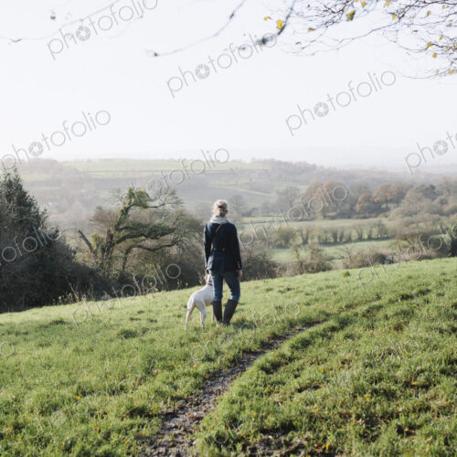 A woman walking with a dog on high ground overlooking the countryside. A woman walking with a dog on high ground overlooking the countryside.