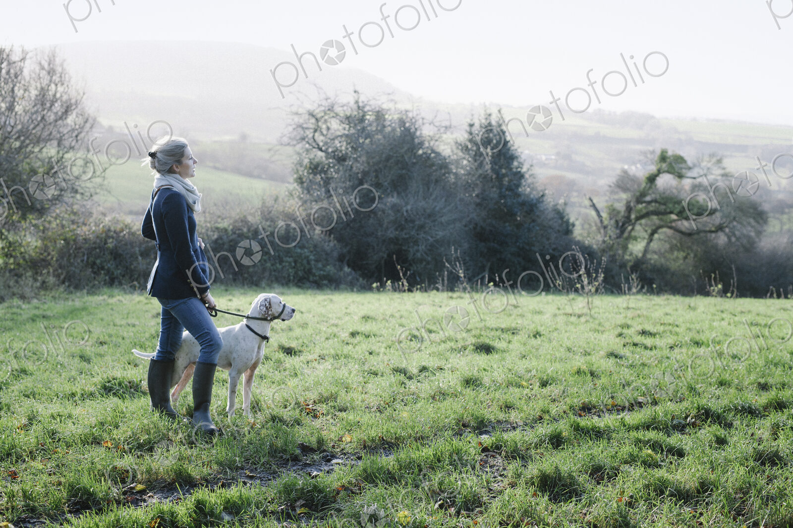 A woman walking with a dog on high ground overlooking the countryside.