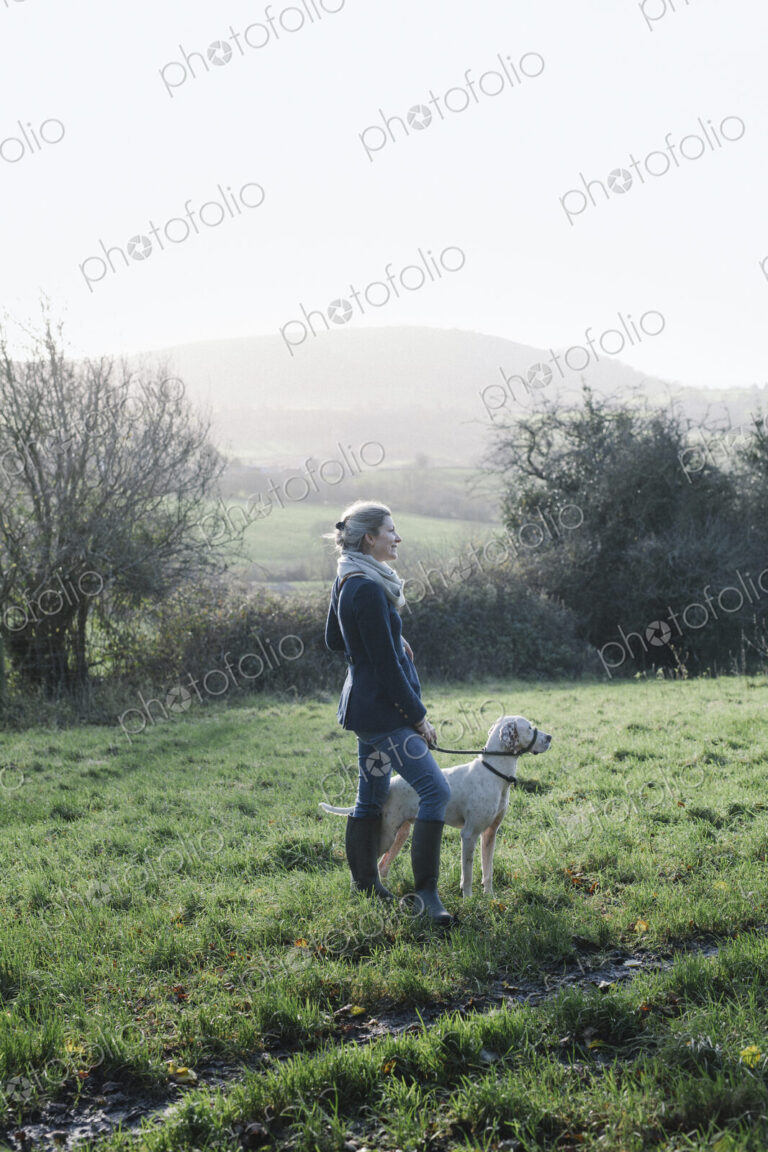 A woman walking with a dog on high ground overlooking the countryside.