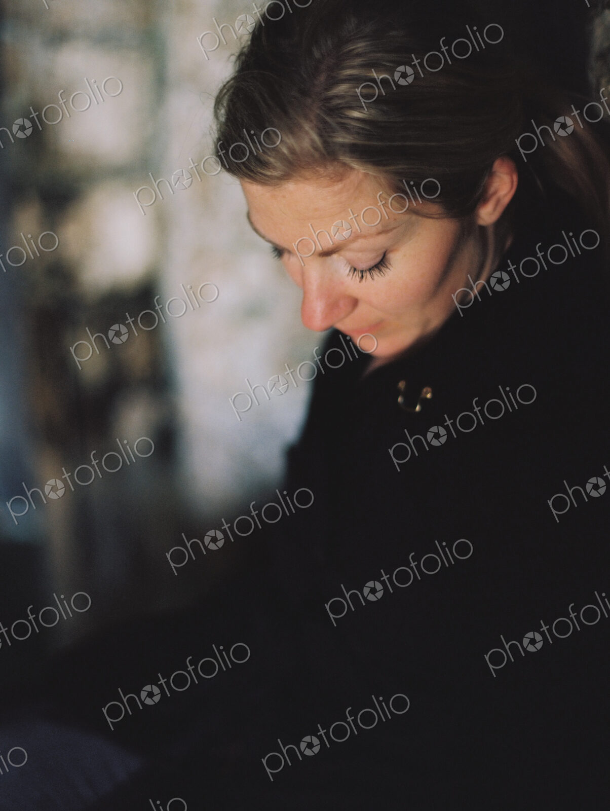 A woman wearing a black coat, looking down in a pensive mood.