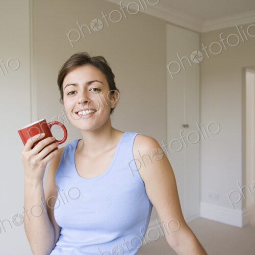 A woman wearing a blue top, seated holding a red china mug.