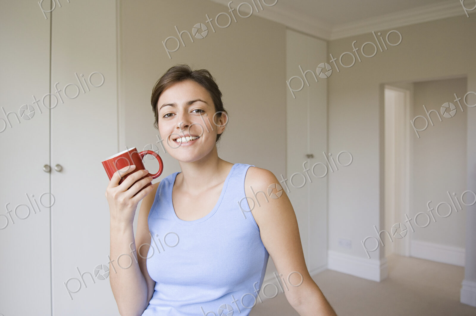 A woman wearing a blue top, seated holding a red china mug.