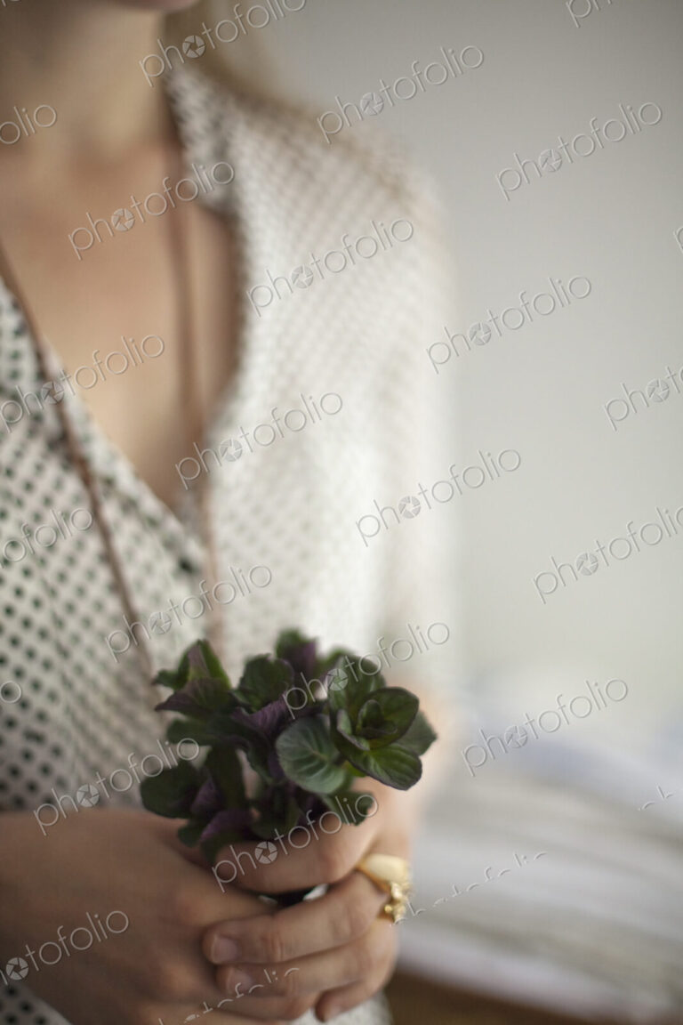 A woman wearing a dress and necklace, holding a small bunch of red and green plant…