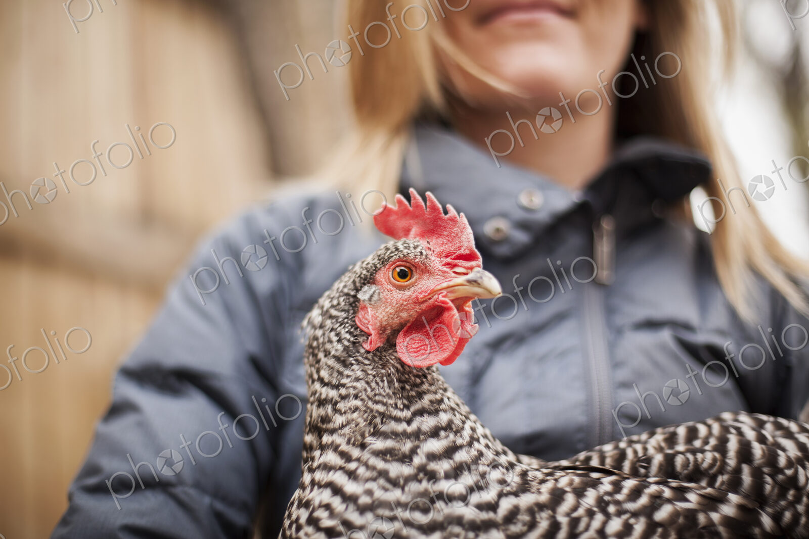 A woman wearing a grey coat and holding a chicken.